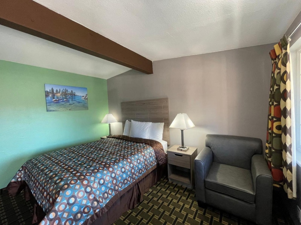 A hotel room with a bed, chair, nightstand, and lamp.