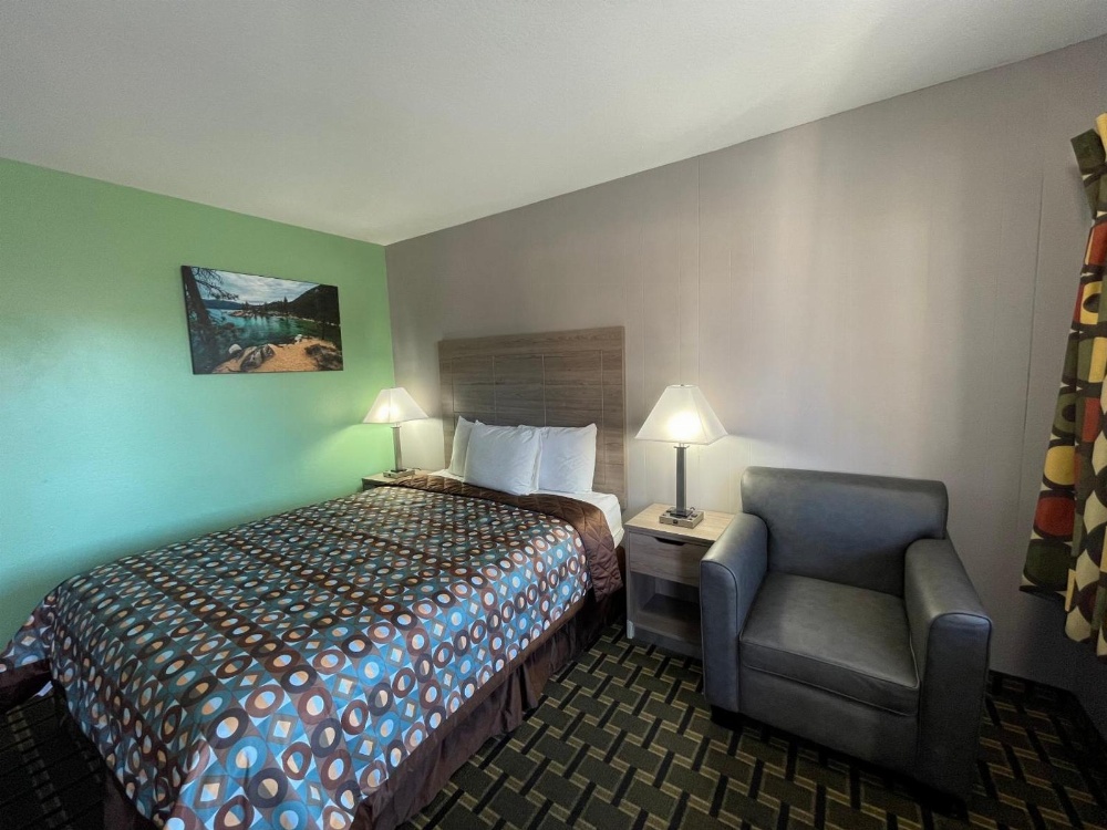 A hotel room with a bed, chair, nightstand, and lamp.