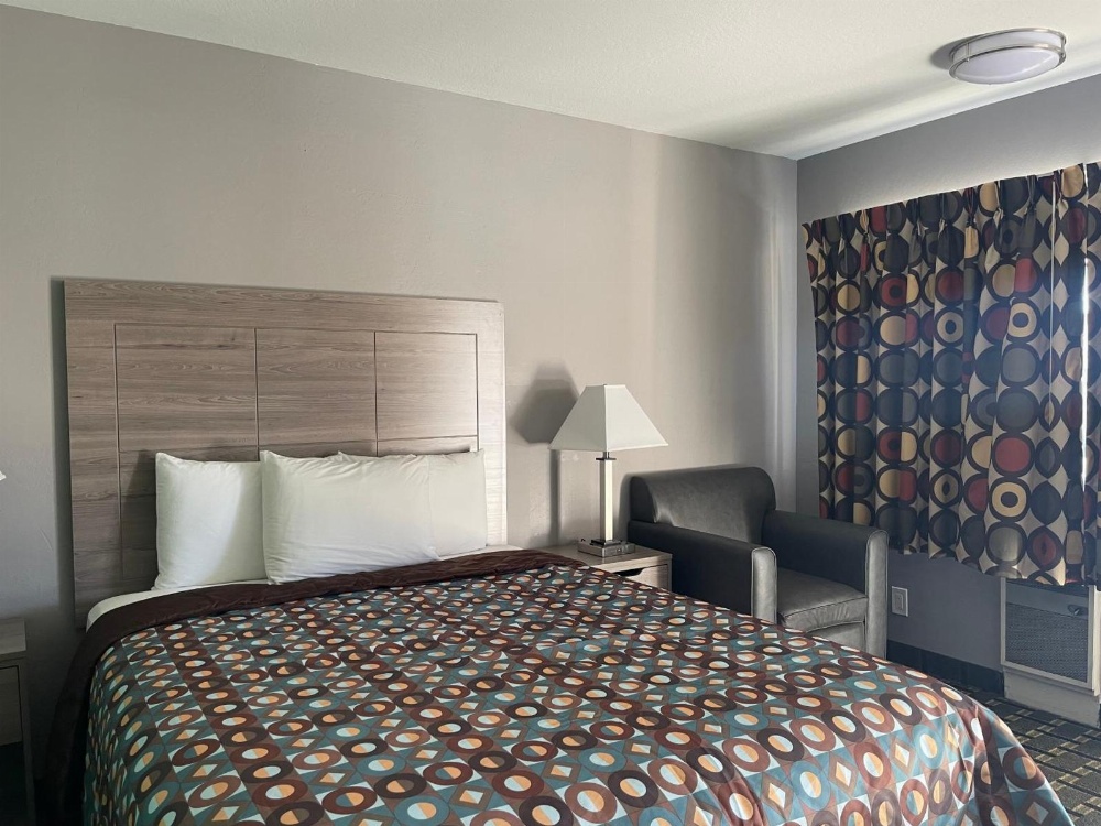 A hotel room with a bed, nightstand, lamp, chair, and window