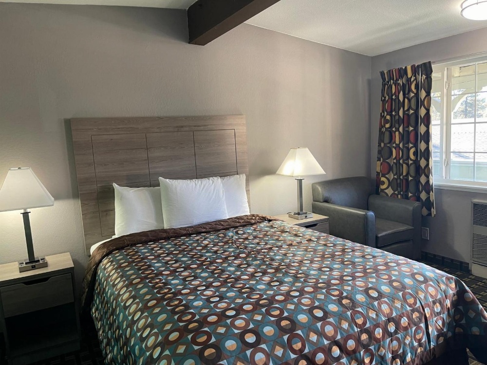 A hotel room with a bed, two nightstands, a chair, and a window.