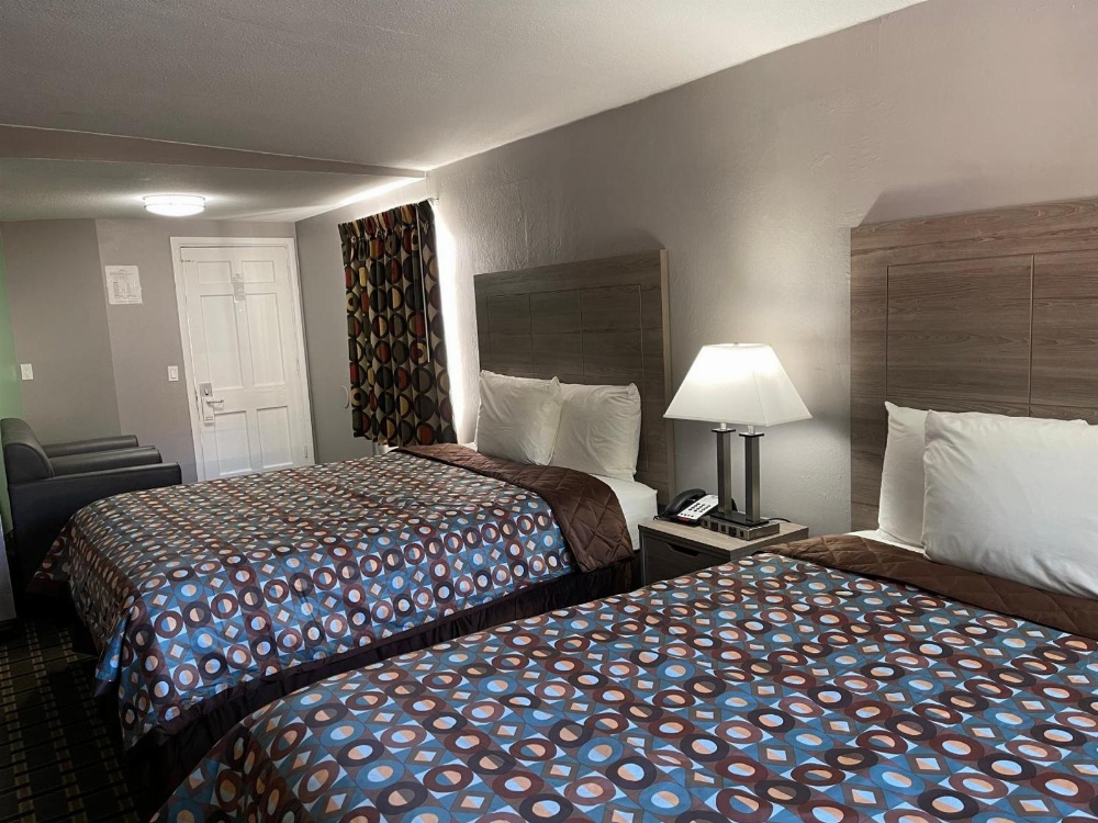 A hotel room with two beds, a nightstand, and a lamp.