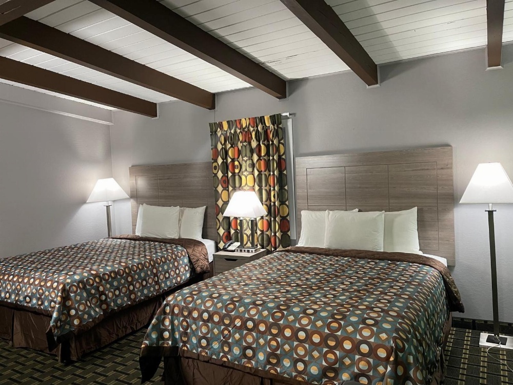 A hotel room with two beds, lamps, and a window with a curtain.
