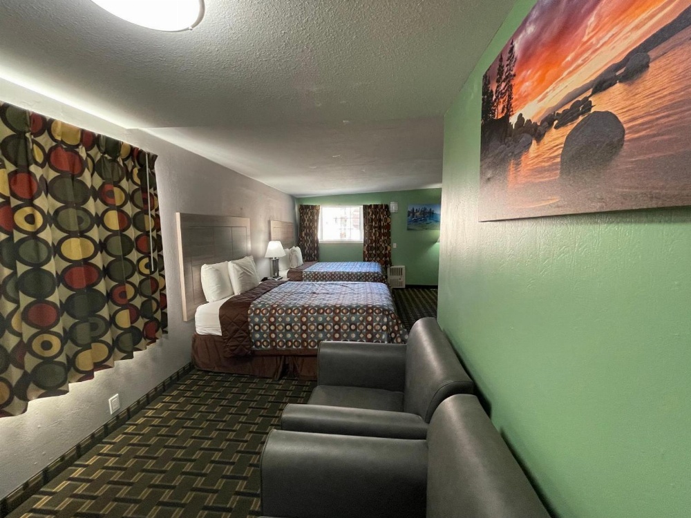 A wide view of a hotel room with two queen beds, a sofa, and a window.