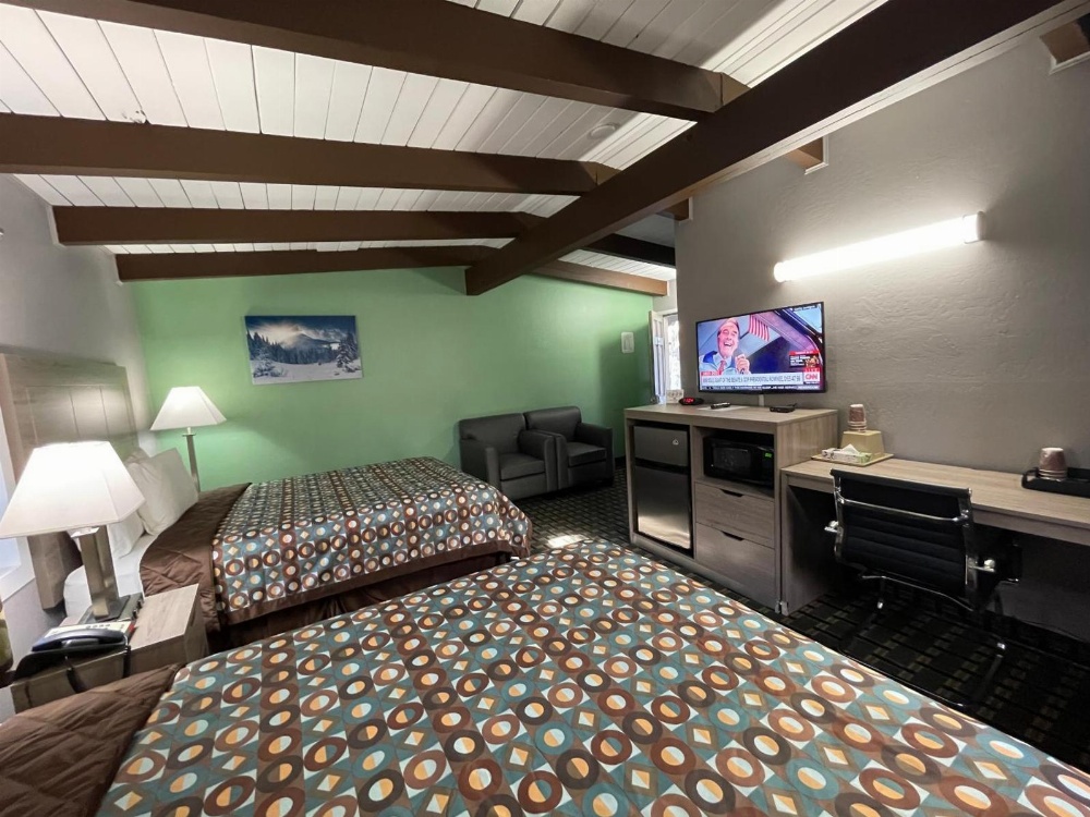 A wide view of a hotel room with two beds, a desk, a TV, and a sitting area.