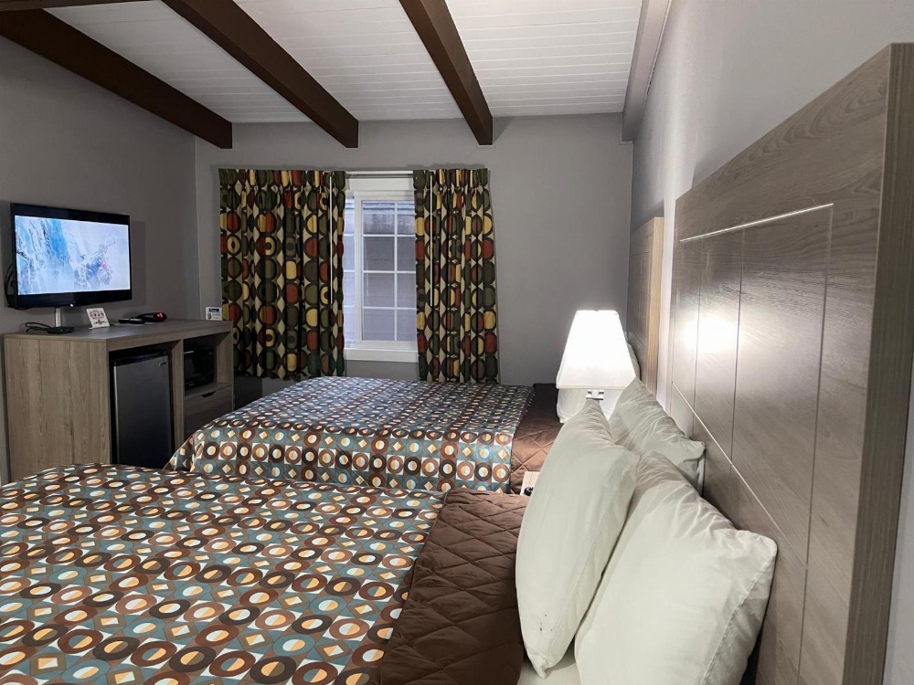 A hotel room with two beds, a TV, a window, and a desk.