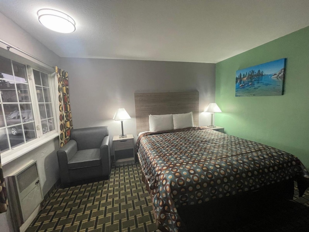 A wide-angle view of a hotel room with a bed, nightstands, a chair, and a window.