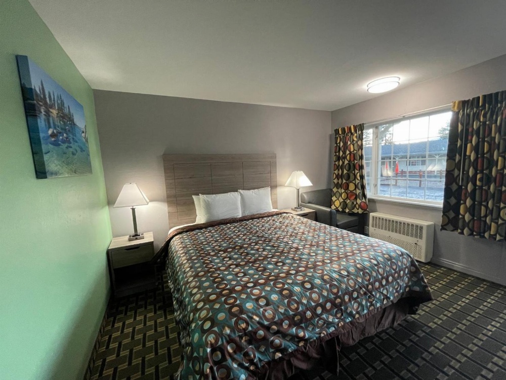 A wide-angle view of a hotel room with a bed, two nightstands, a chair, and a window.