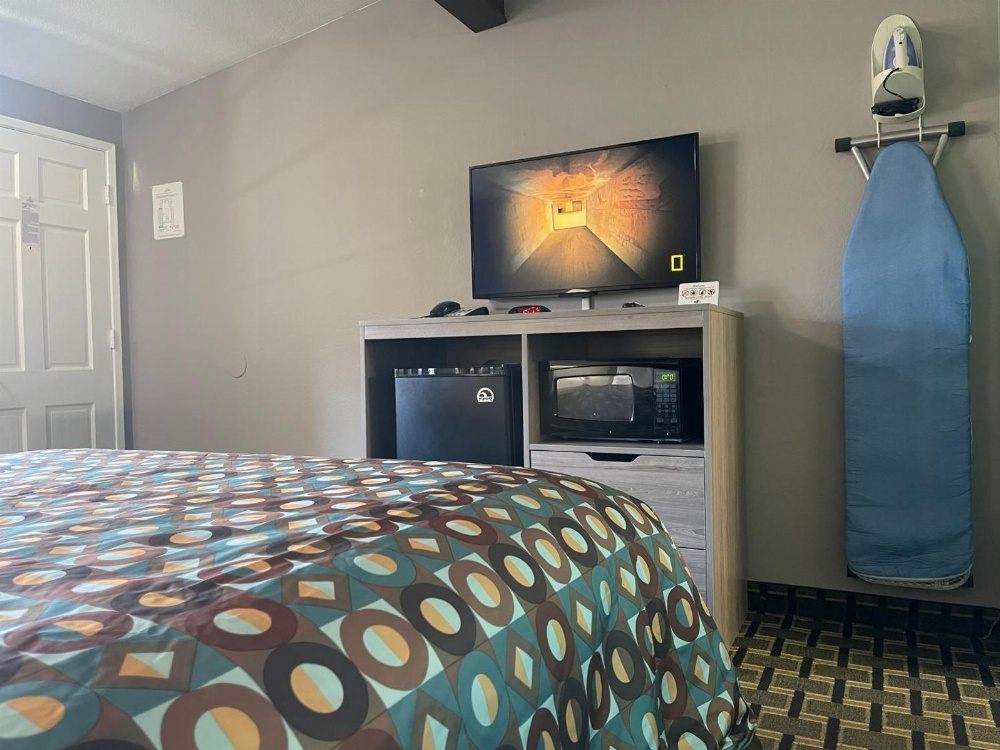 A hotel room with a bed, TV, mini-fridge, microwave, and iron board.