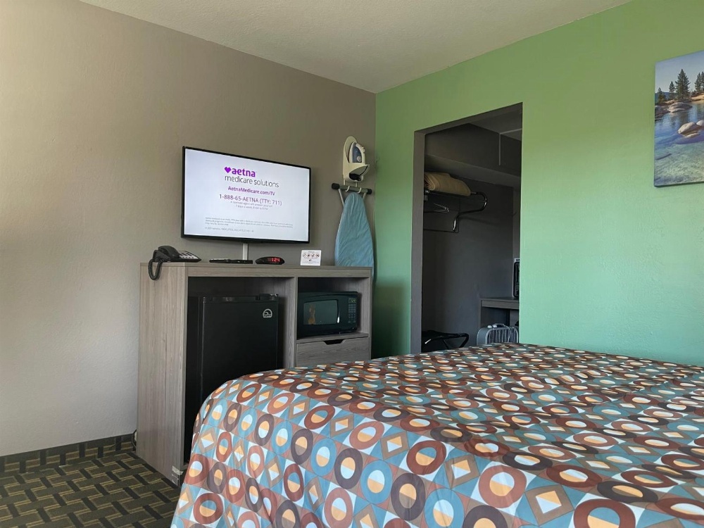 A hotel room with a bed, TV, minifridge, and microwave