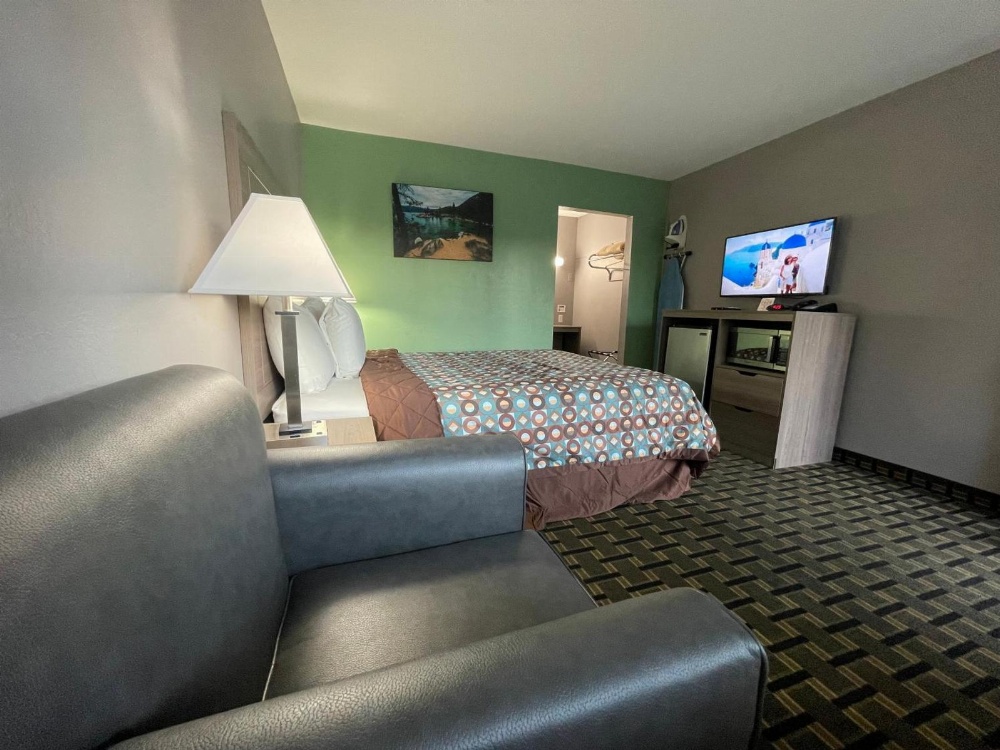 A wide view of a hotel room with a sofa, bed, TV, and lamp.