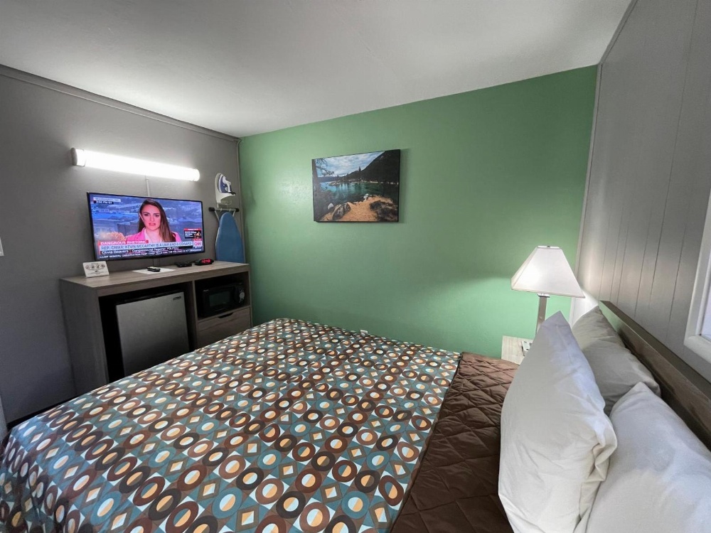 A wide-angle view of a hotel room with a bed, TV, and lamp.