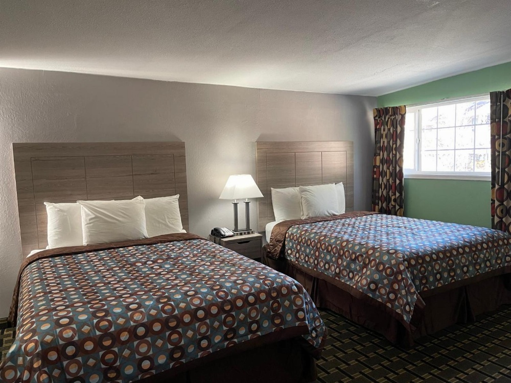 A hotel room with two beds, a nightstand, and a window.