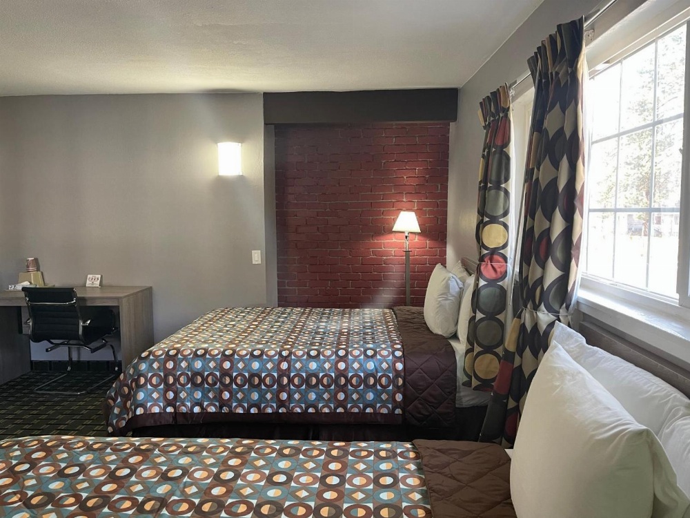 A hotel room with two beds, a desk, and a window.